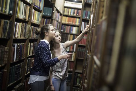 Two female students pick a book from the shelves at a library